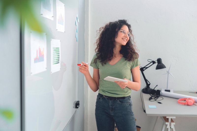 Junge Frau steht mit Stift an einem Whiteboard
